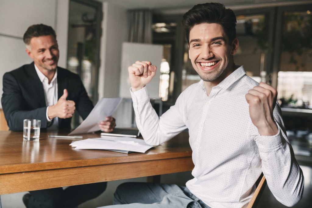 Career, office and placement concept - successful caucasian man 30s rejoicing and clenching fists, during job interview with employee of big company