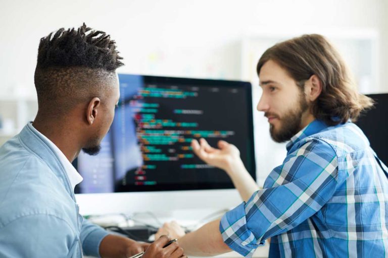 One of software developers pointing at computer screen while explaining his co-worker new method of data decoding