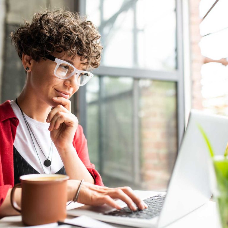 Busy young elegant woman in eyeglasses looking at laptop display